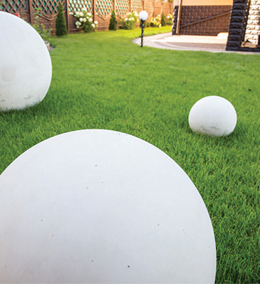 Ceramiczne białe kule w różnych rozmiarach w ogrodzie, w tle widać lampę ogrodową.